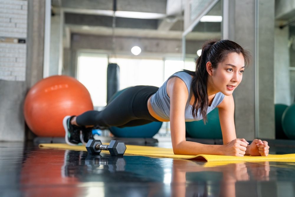 A girl does a plank on a yellow yoga mat.