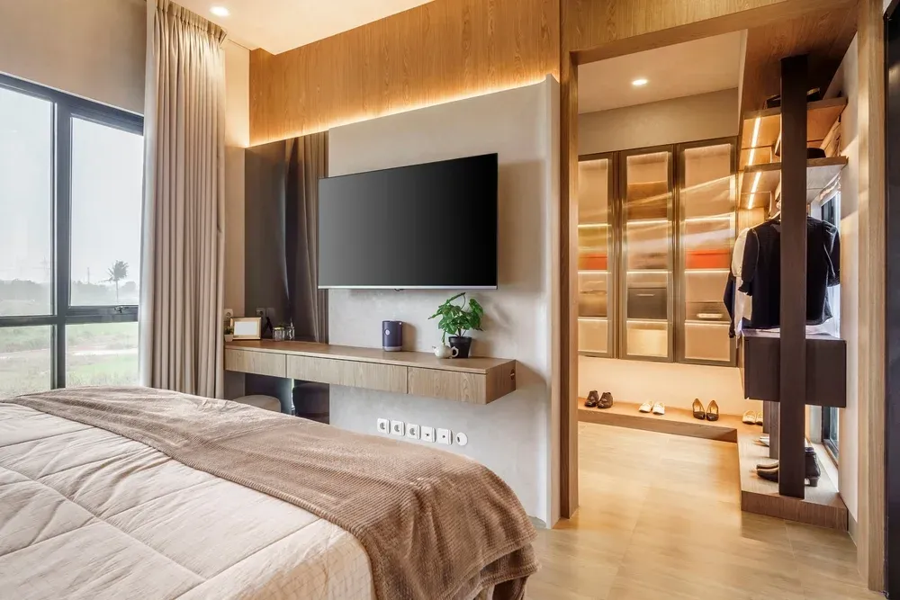 Spacious bedroom with a wall-mounted TV over a floating console and a large window.
